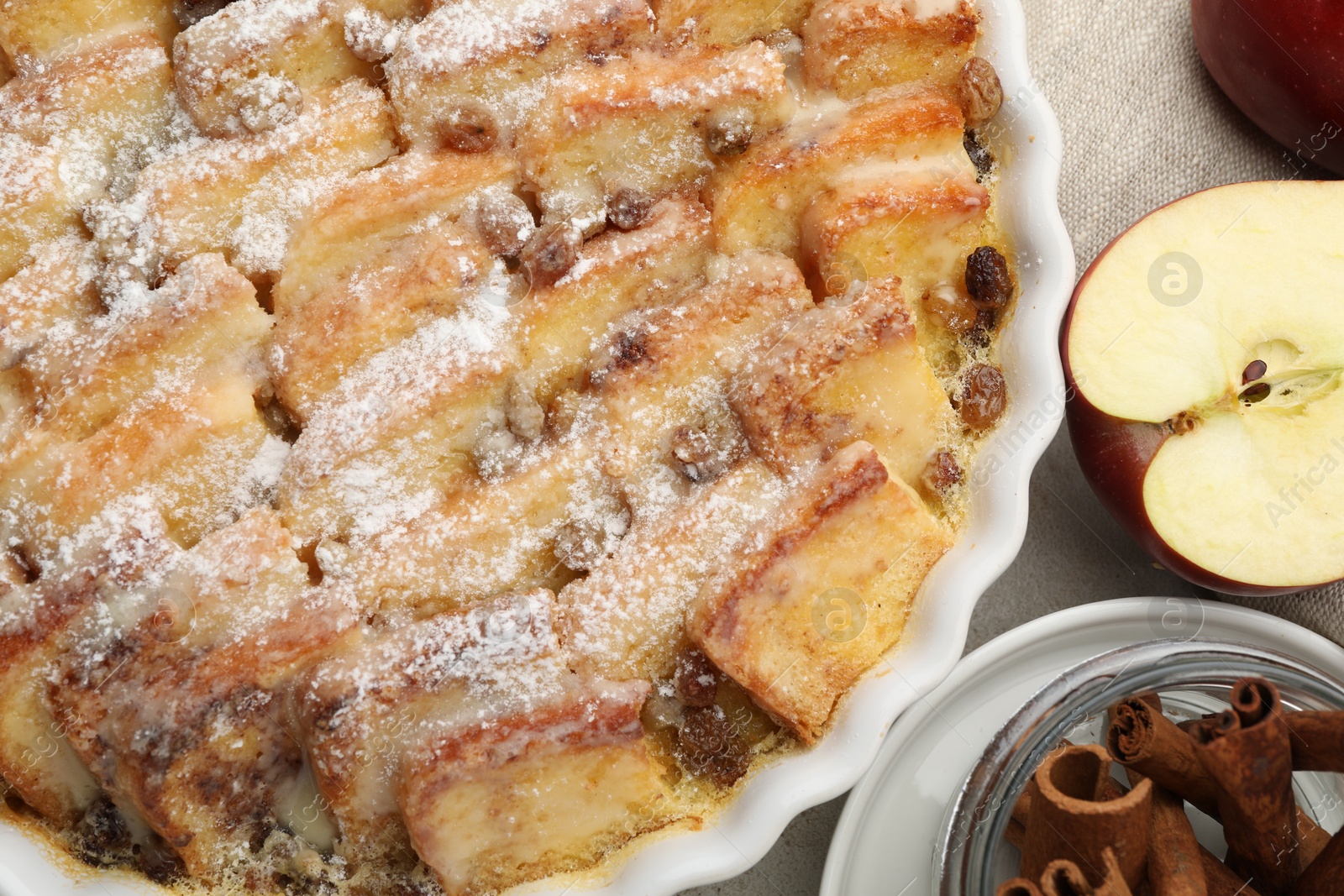 Photo of Delicious bread pudding with raisins, powdered sugar, cinnamon and apples on grey table, flat lay