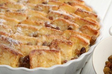 Photo of Delicious bread pudding with raisins and powdered sugar on white wooden table, closeup