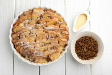 Photo of Delicious bread pudding with raisins, powdered sugar, condensed milk on white wooden table, flat lay