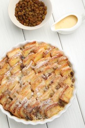 Photo of Delicious bread pudding with raisins, powdered sugar, condensed milk on white wooden table, flat lay