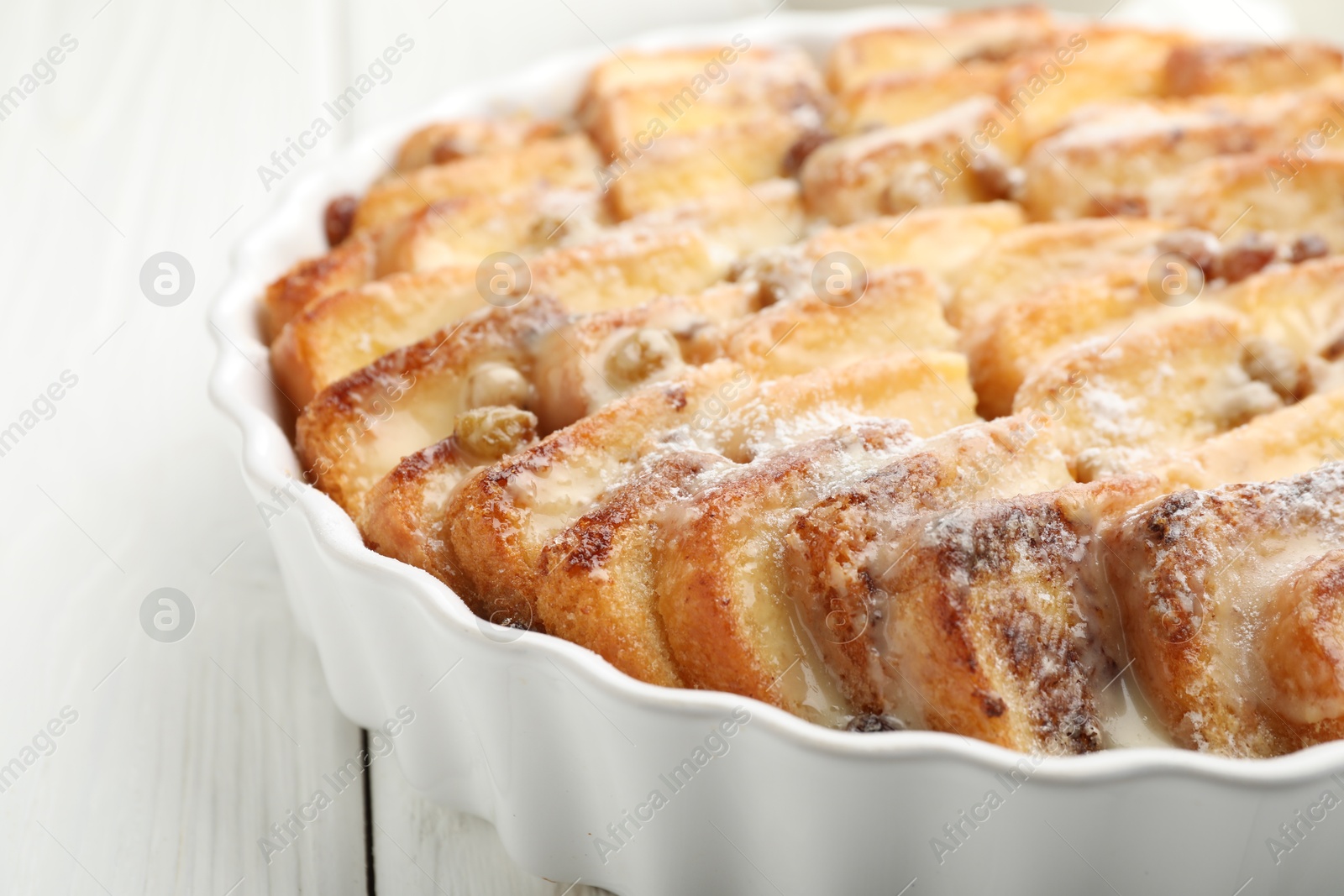 Photo of Delicious bread pudding with raisins and powdered sugar on white wooden table, closeup