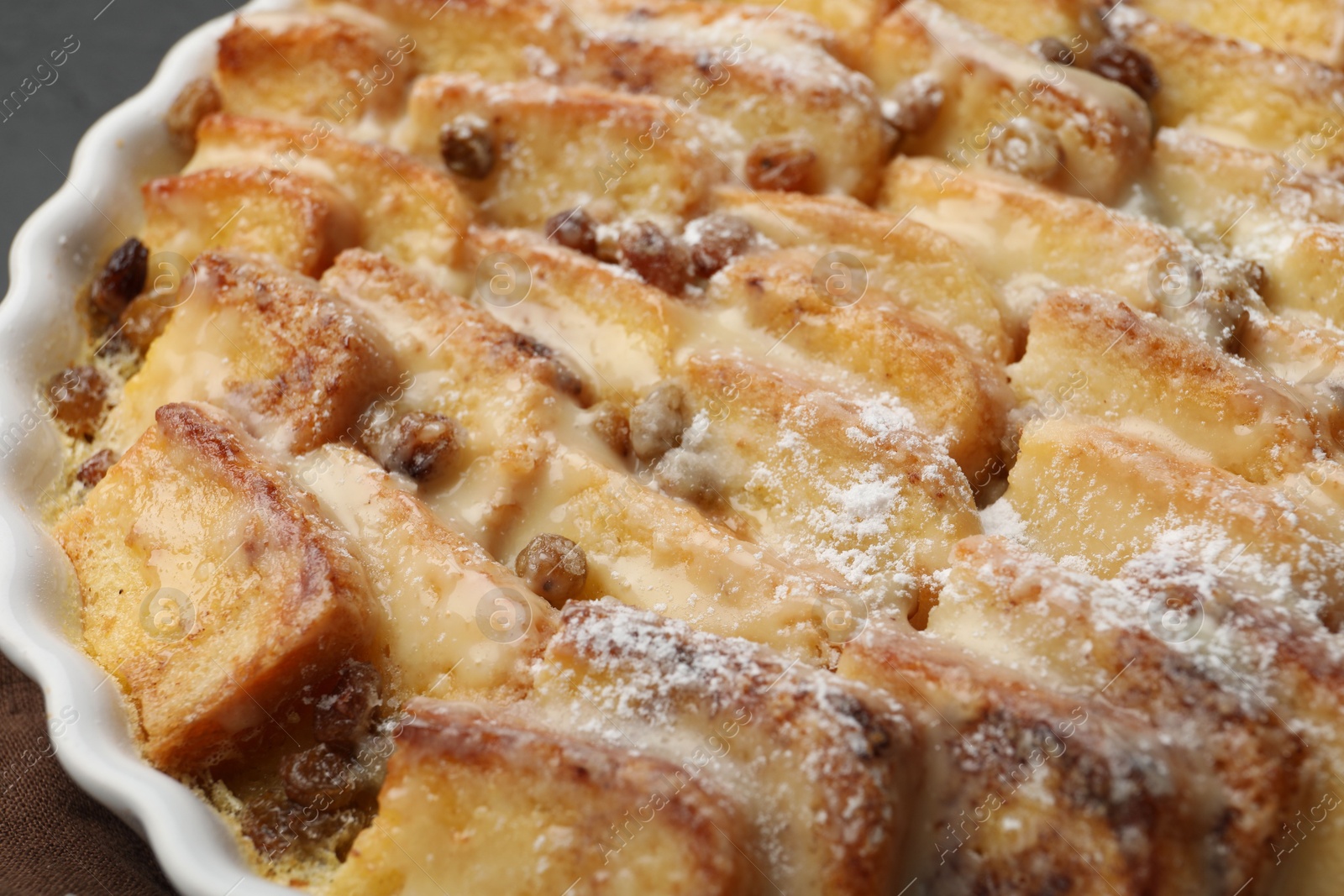 Photo of Delicious bread pudding with raisins and powdered sugar in dish, closeup