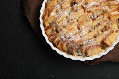 Photo of Delicious bread pudding with raisins and powdered sugar on black table, top view. Space for text