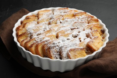 Photo of Delicious bread pudding with raisins and powdered sugar on black table, closeup