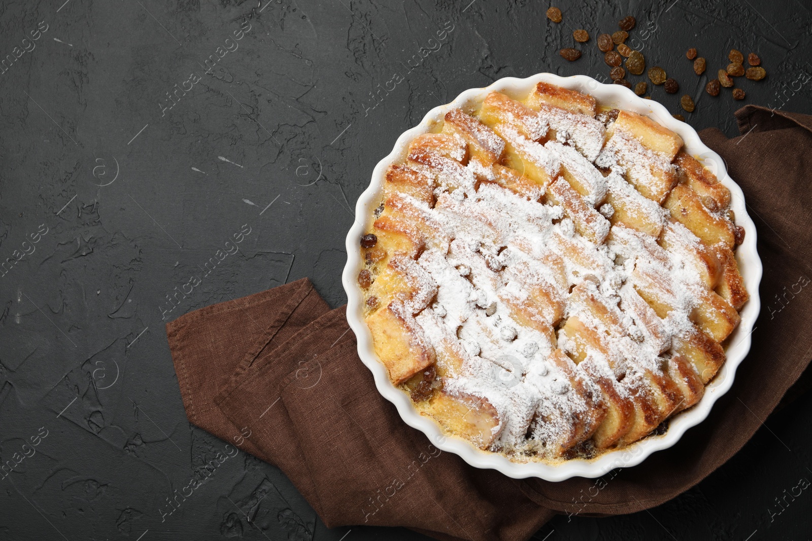 Photo of Delicious bread pudding with raisins and powdered sugar on black table, top view. Space for text