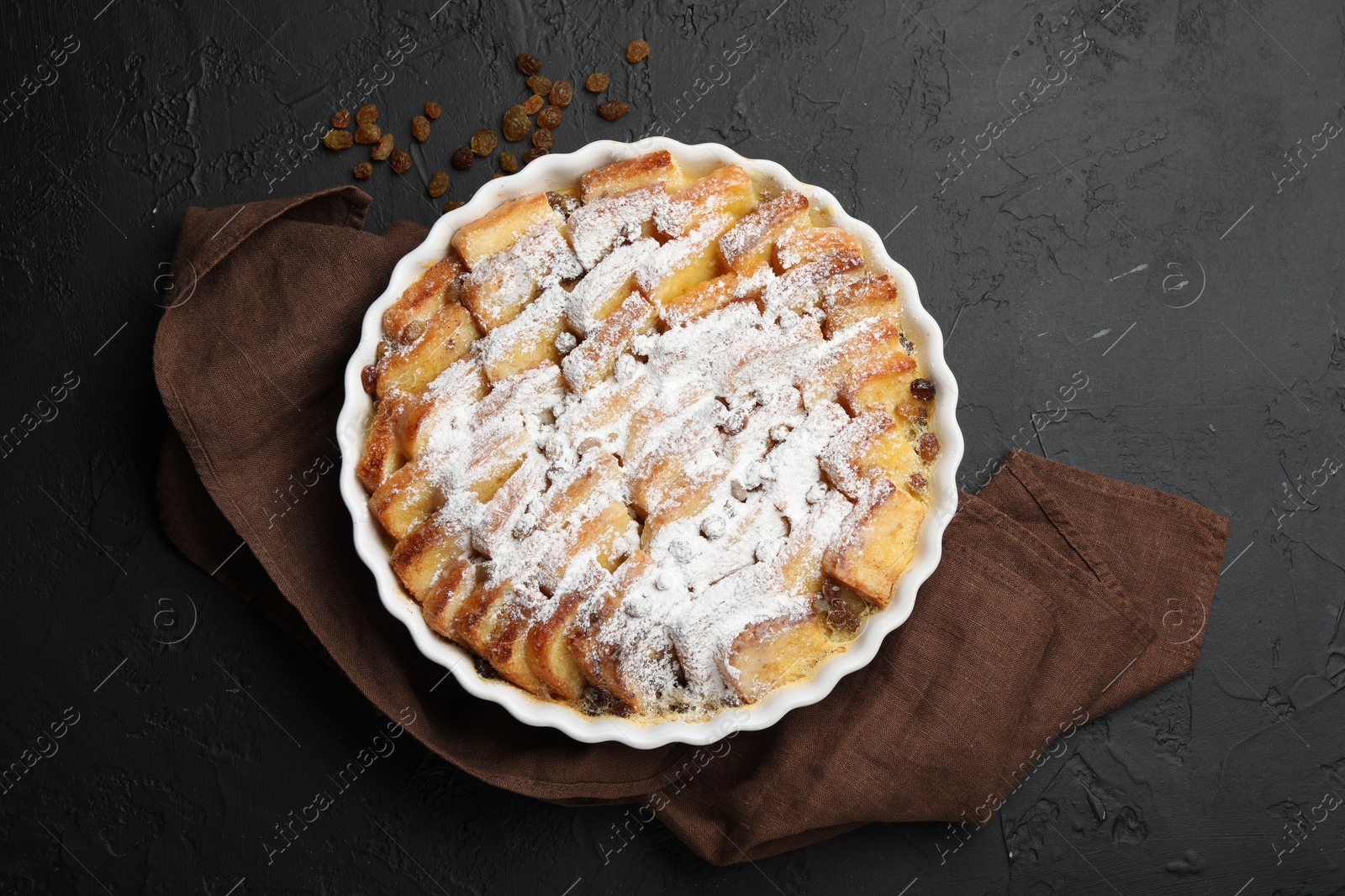 Photo of Delicious bread pudding with raisins and powdered sugar on black table, top view