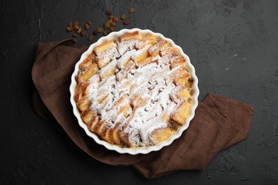 Photo of Delicious bread pudding with raisins and powdered sugar on black table, top view