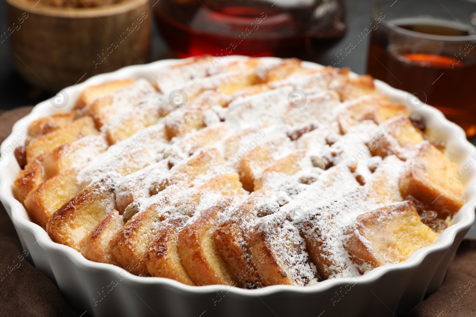 Photo of Delicious bread pudding with raisins and powdered sugar on table, closeup