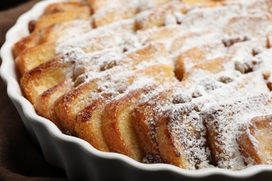 Photo of Delicious bread pudding with raisins and powdered sugar in dish, closeup