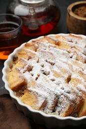 Photo of Delicious bread pudding with raisins, powdered sugar and tea on table, closeup