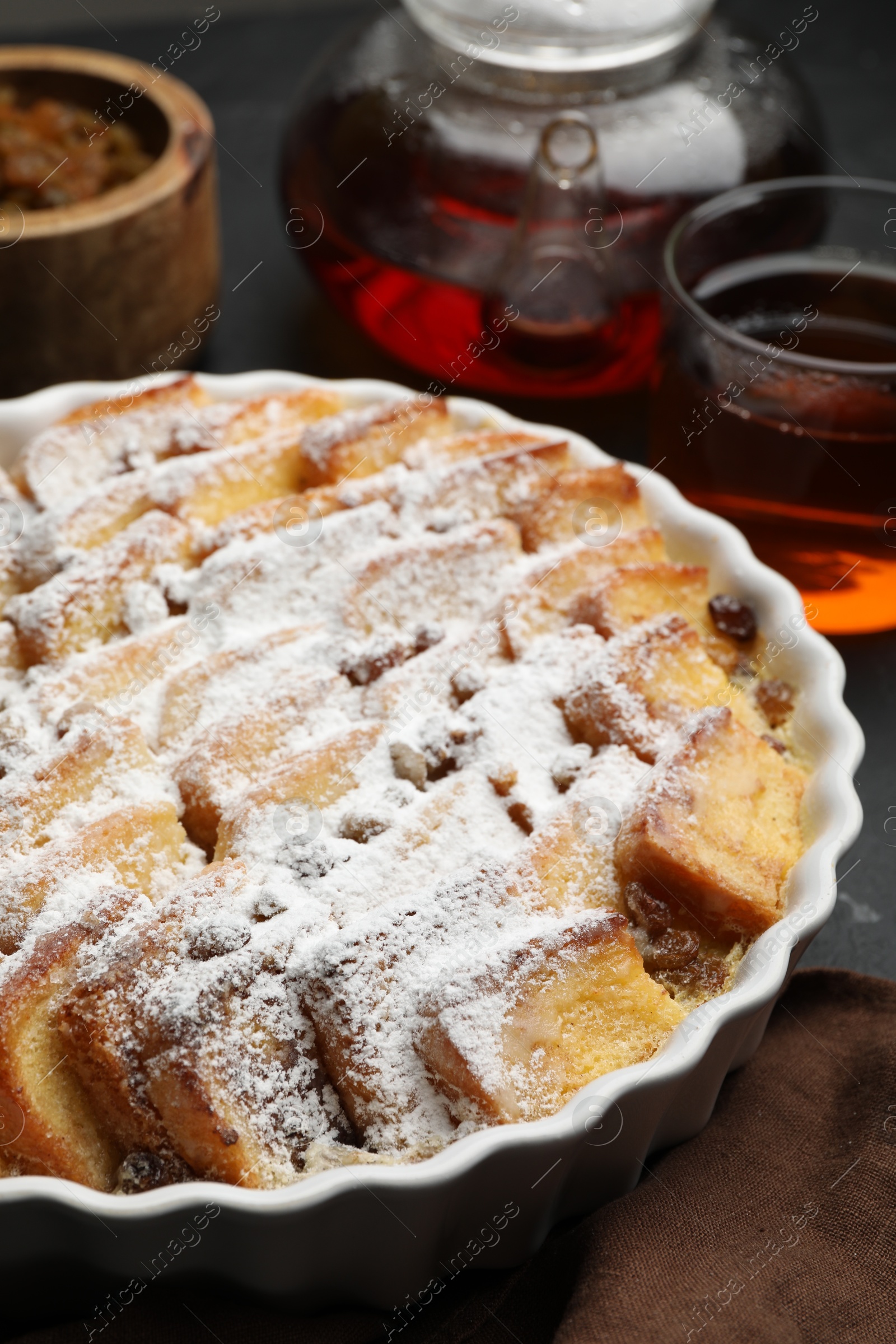 Photo of Delicious bread pudding with raisins, powdered sugar and tea on table, closeup