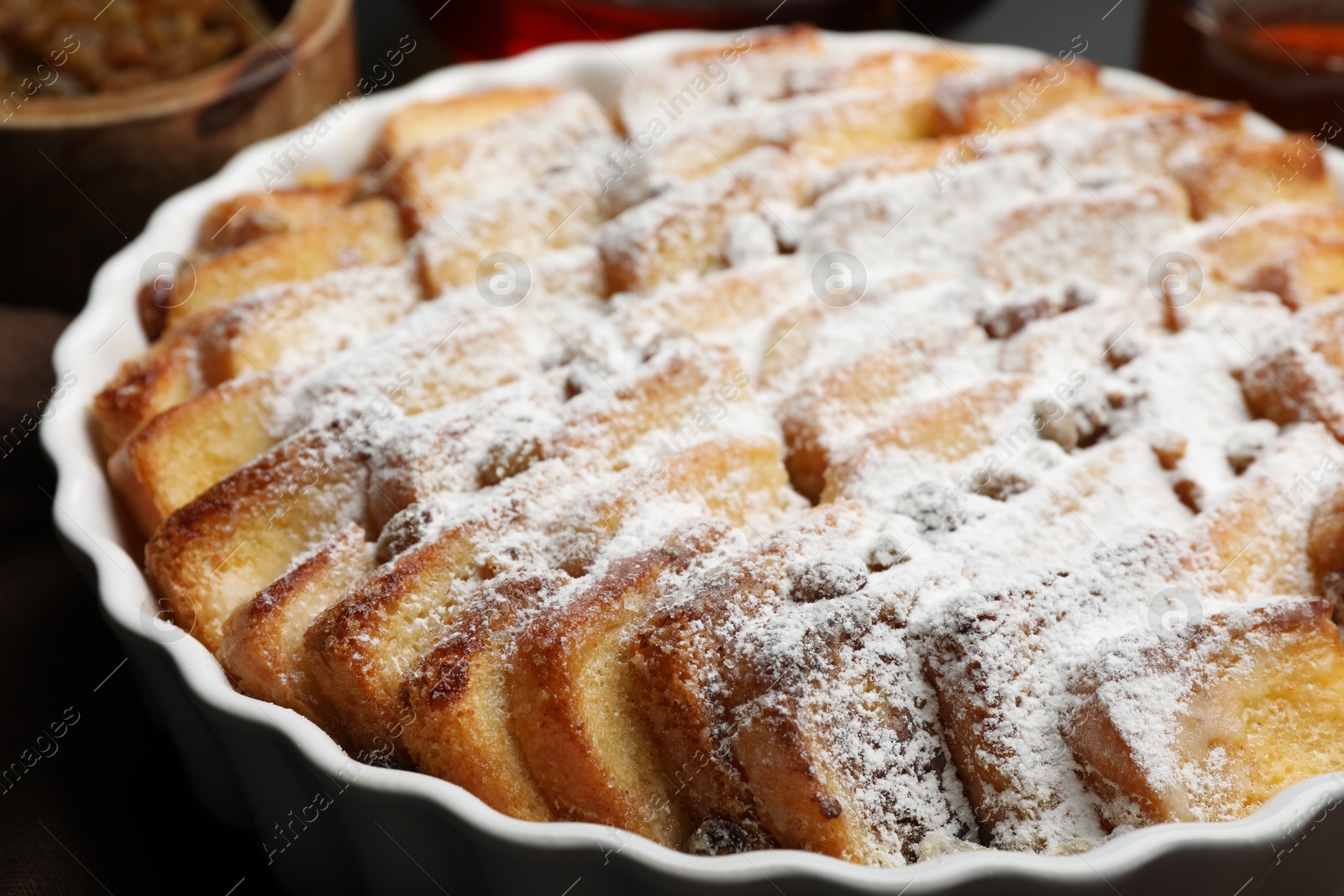 Photo of Delicious bread pudding with raisins and powdered sugar in dish, closeup