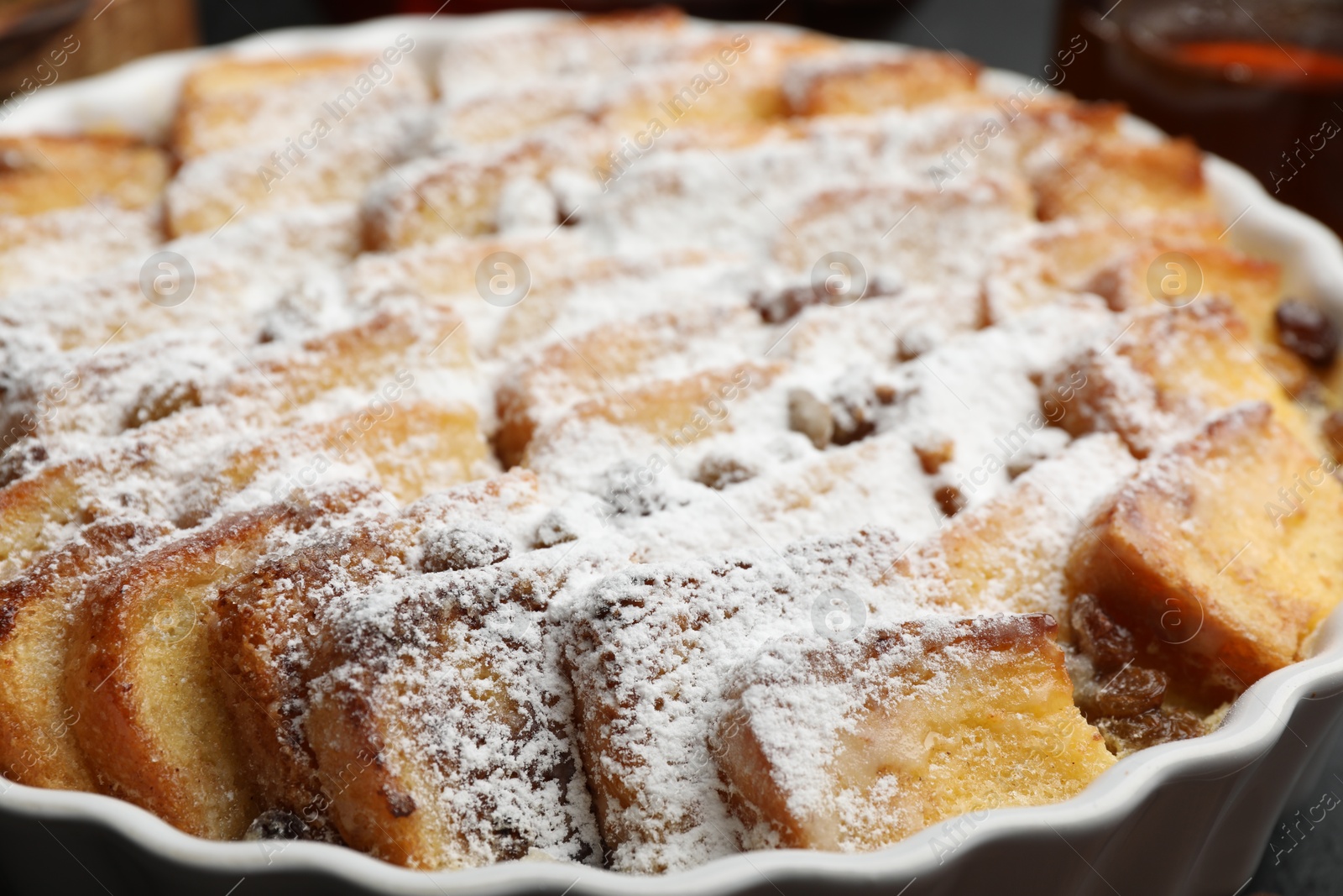 Photo of Delicious bread pudding with raisins and powdered sugar in dish, closeup