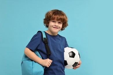 Little boy with soccer ball and backpack on light blue background