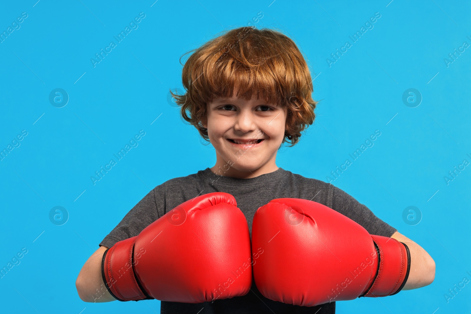 Photo of Little boy with boxing gloves on light blue background