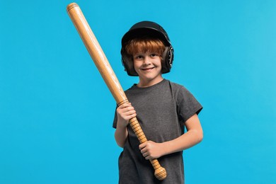 Little boy in helmet with baseball bat on light blue background