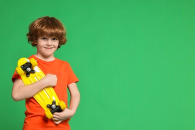 Little boy with penny board on light green background, space for text