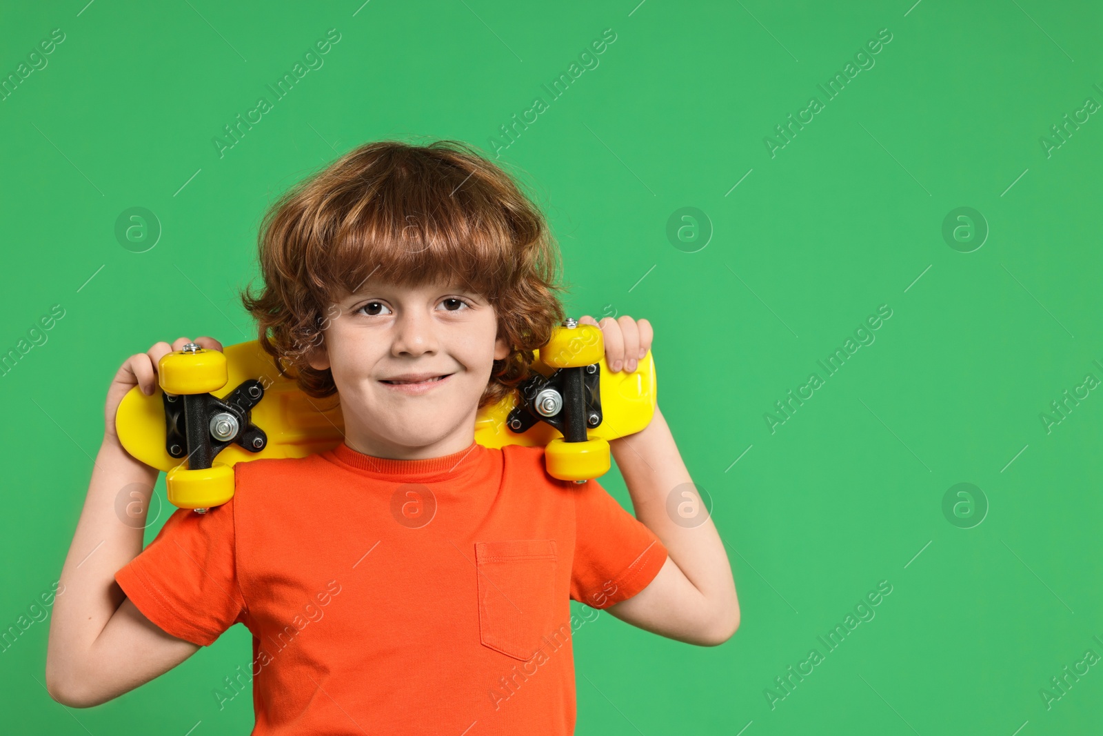 Photo of Little boy with penny board on light green background, space for text