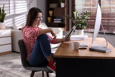 Photo of Happy woman working at desk with computer indoors. Home office