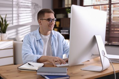 Photo of Happy man working with computer at desk indoors. Home office