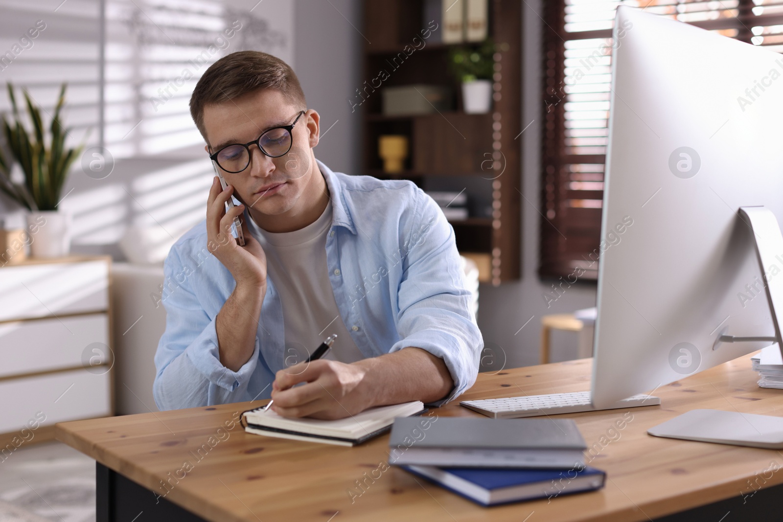 Photo of Handsome man talking by smartphone at desk with computer indoors. Home office