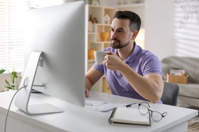 Handsome man working with computer at desk indoors. Home office