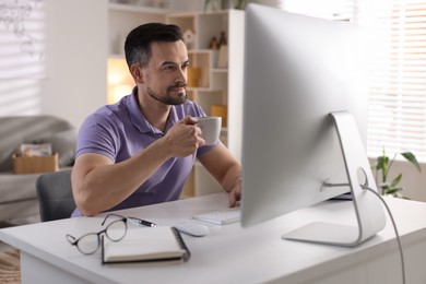 Handsome man working with computer at desk indoors. Home office