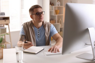 Handsome man working with computer at desk indoors. Home office