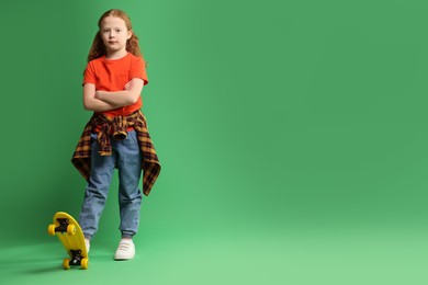 Photo of Stylish little girl with penny board on green background, space for text