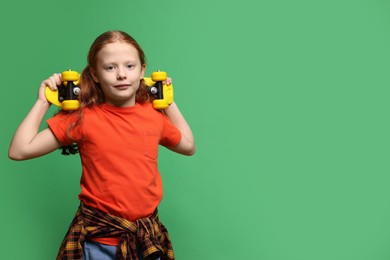 Photo of Stylish little girl with penny board on green background, space for text