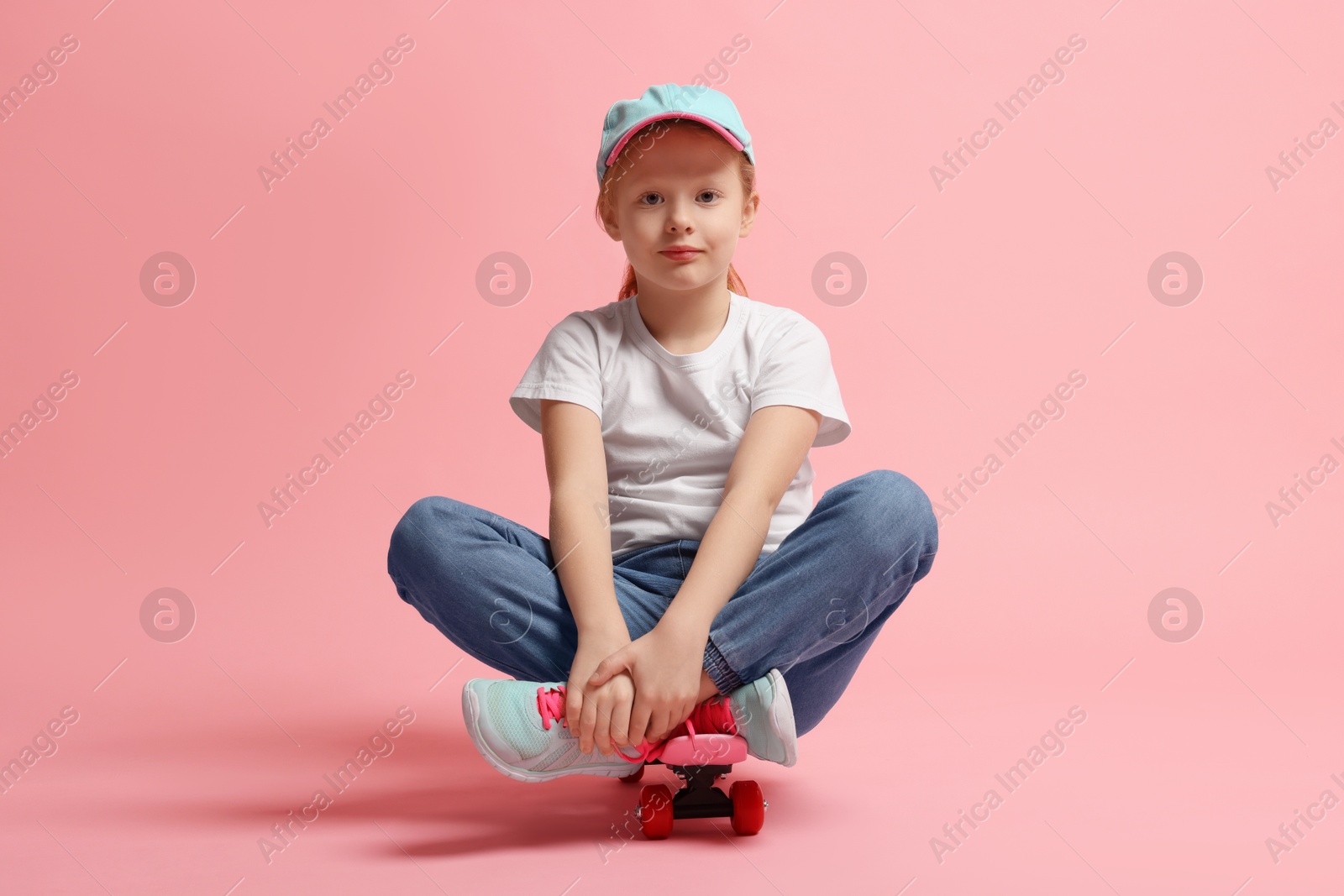 Photo of Little girl sitting on penny board against pink background