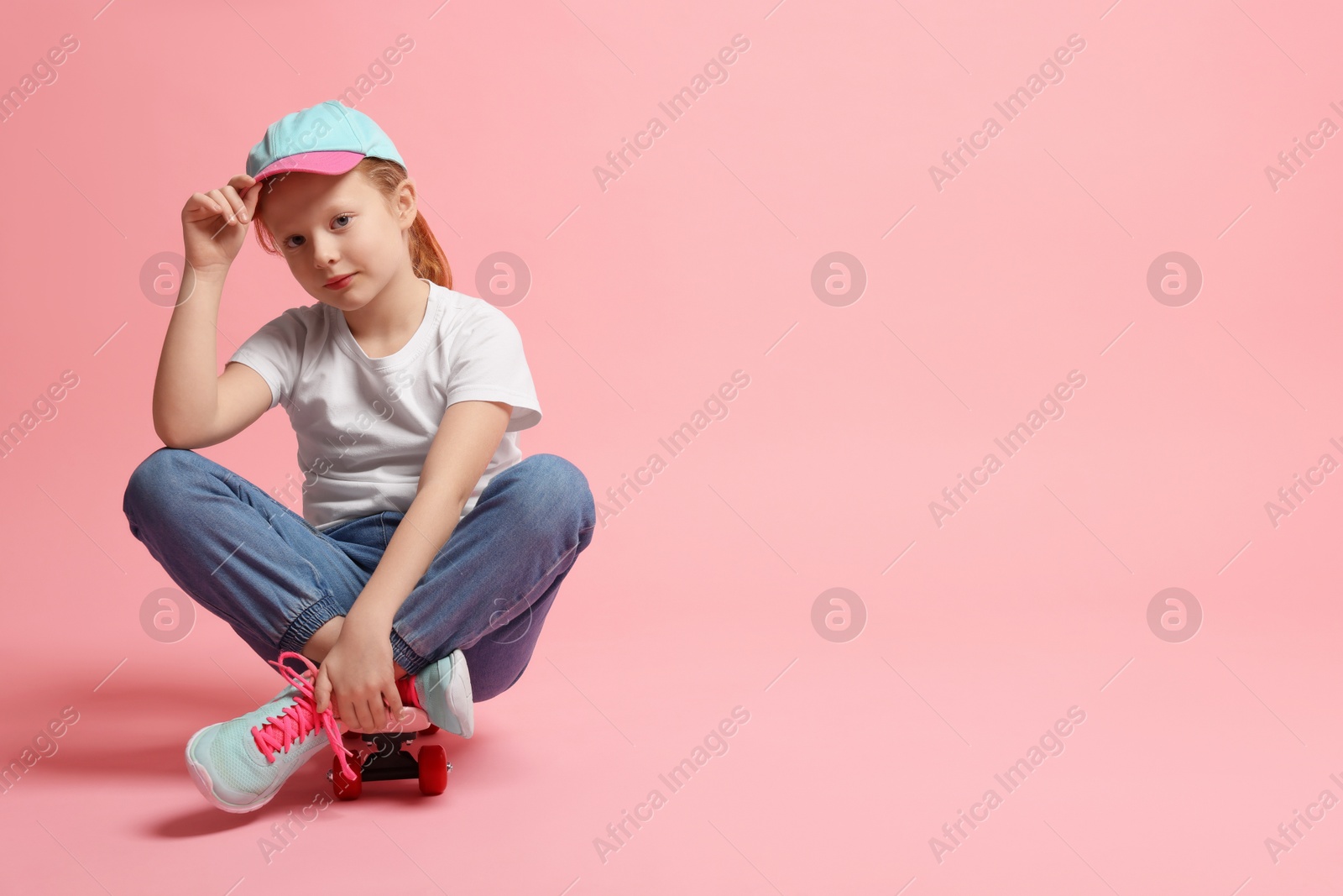 Photo of Little girl sitting on penny board against pink background, space for text