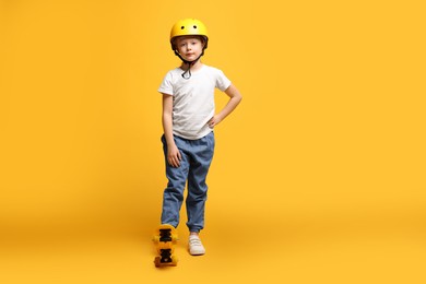 Little girl in helmet with penny board on orange background