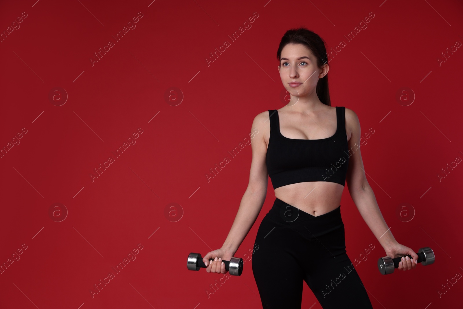 Photo of Woman in sportswear exercising with dumbbells on red background, space for text