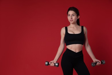 Photo of Woman in sportswear exercising with dumbbells on red background, space for text