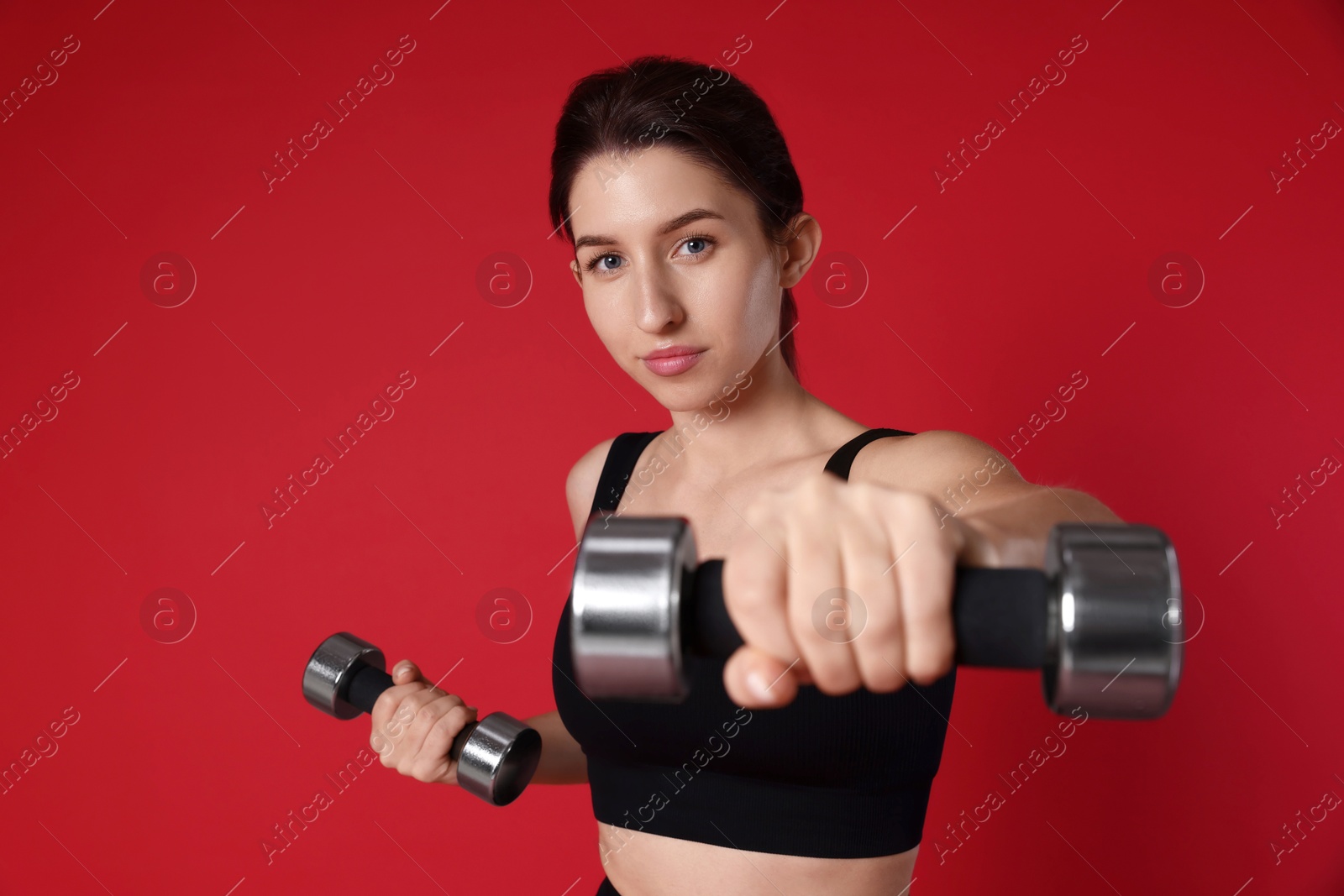 Photo of Woman in sportswear exercising with dumbbells on red background