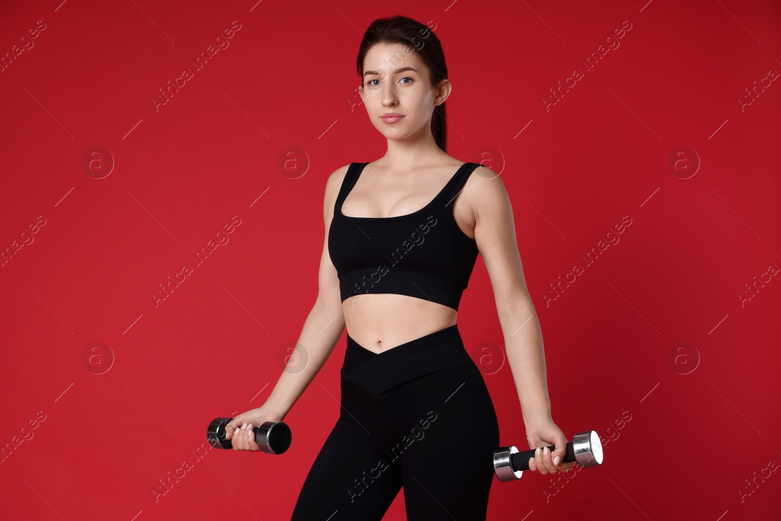 Photo of Woman in sportswear exercising with dumbbells on red background