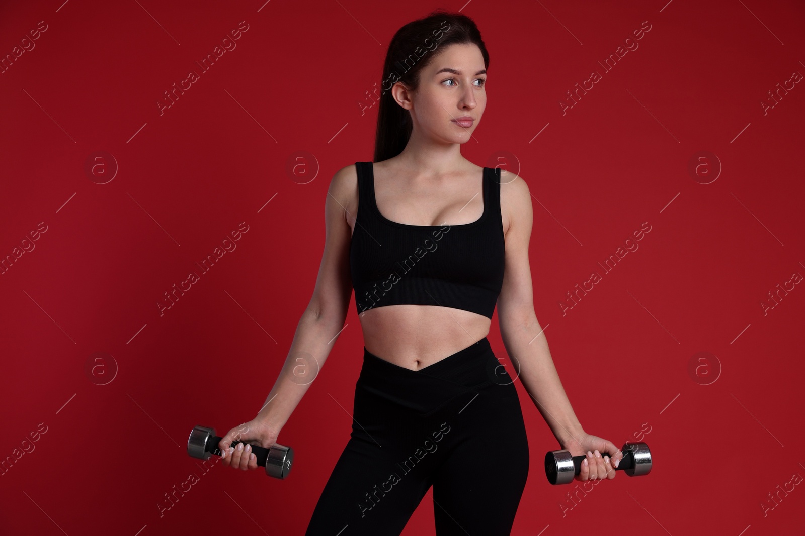 Photo of Woman in sportswear exercising with dumbbells on red background