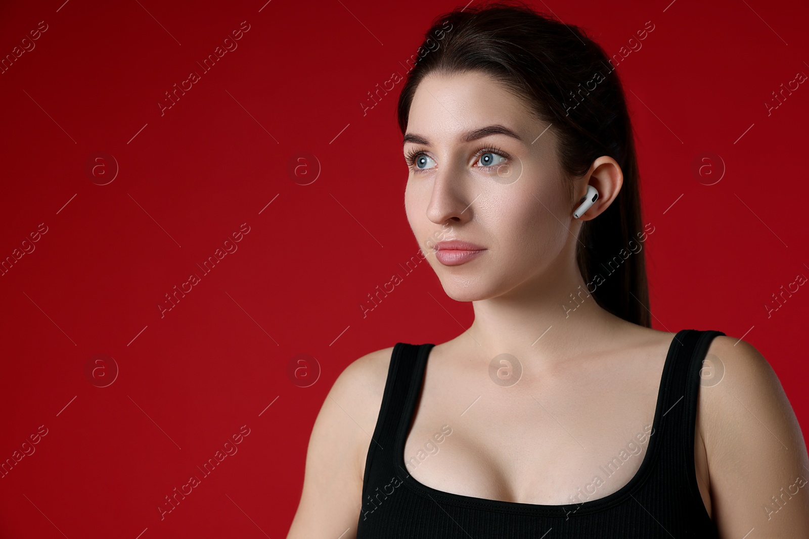 Photo of Woman in sportswear with wireless earphone on red background, space for text