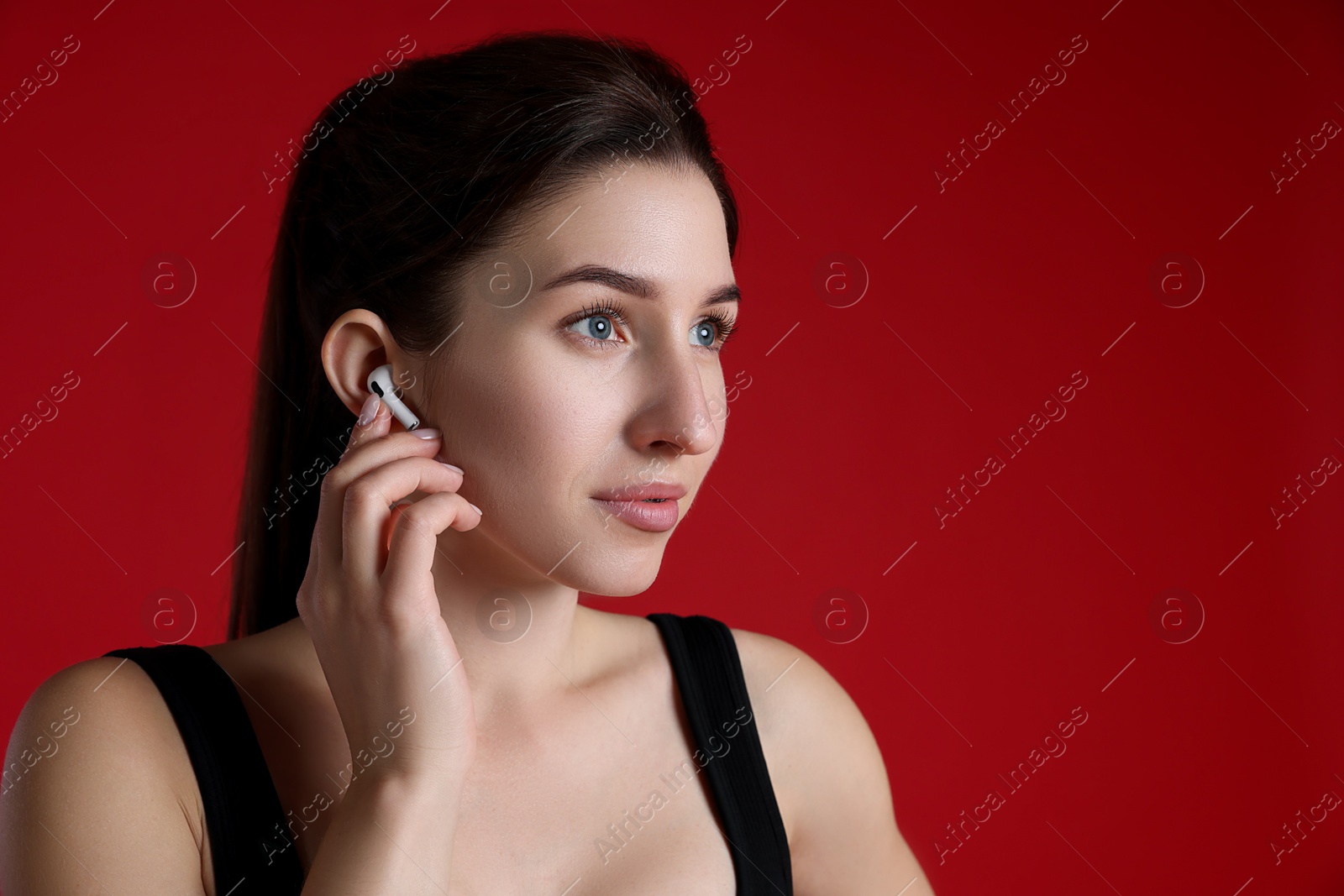 Photo of Woman in sportswear with wireless earphone on red background, space for text