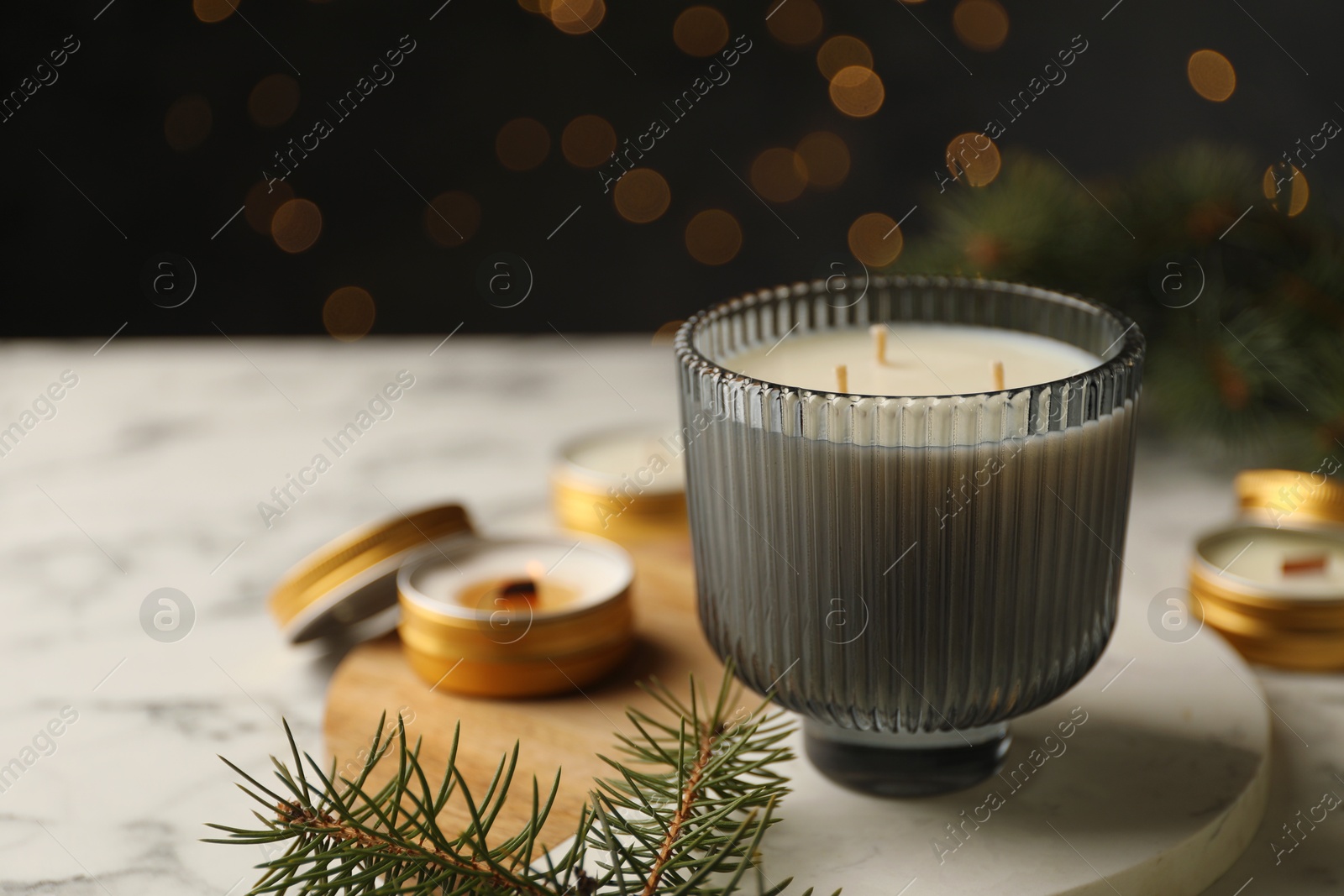 Photo of Soy candles and green fir branches on white marble table, closeup. Space for text