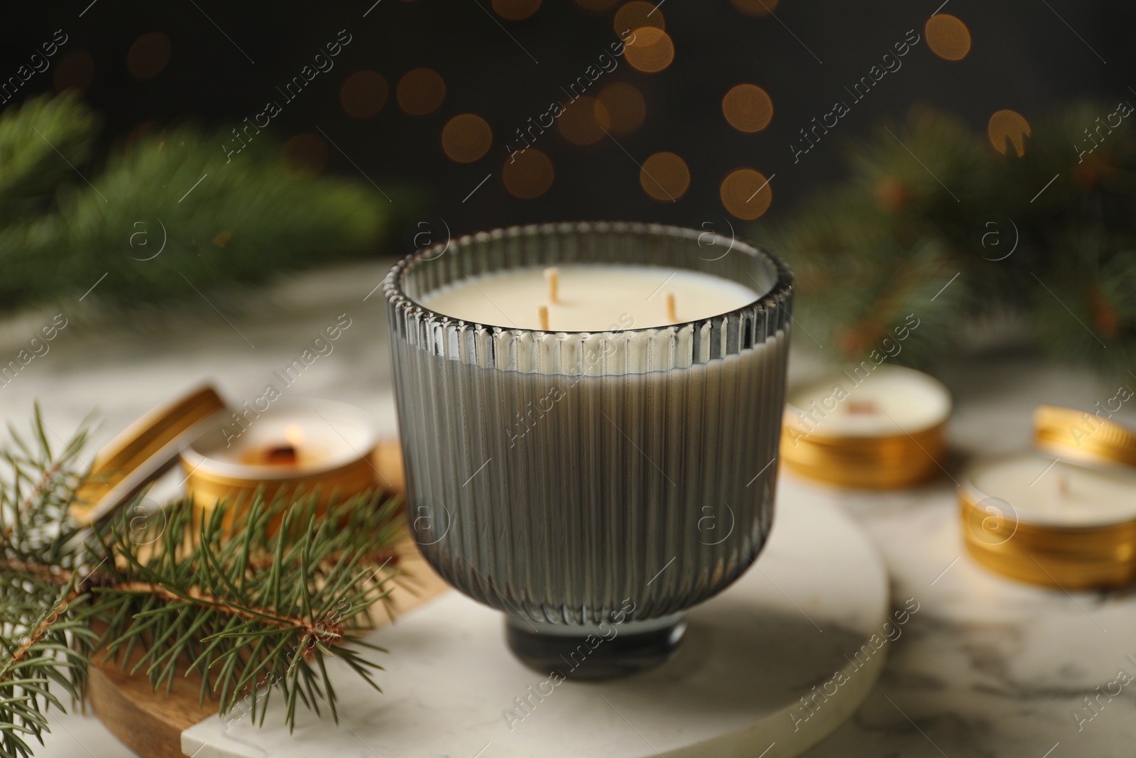 Photo of Soy candles and green fir branches on white marble table, closeup