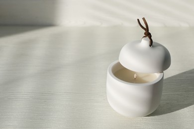 Photo of Soy candle and lid on white wooden table, space for text