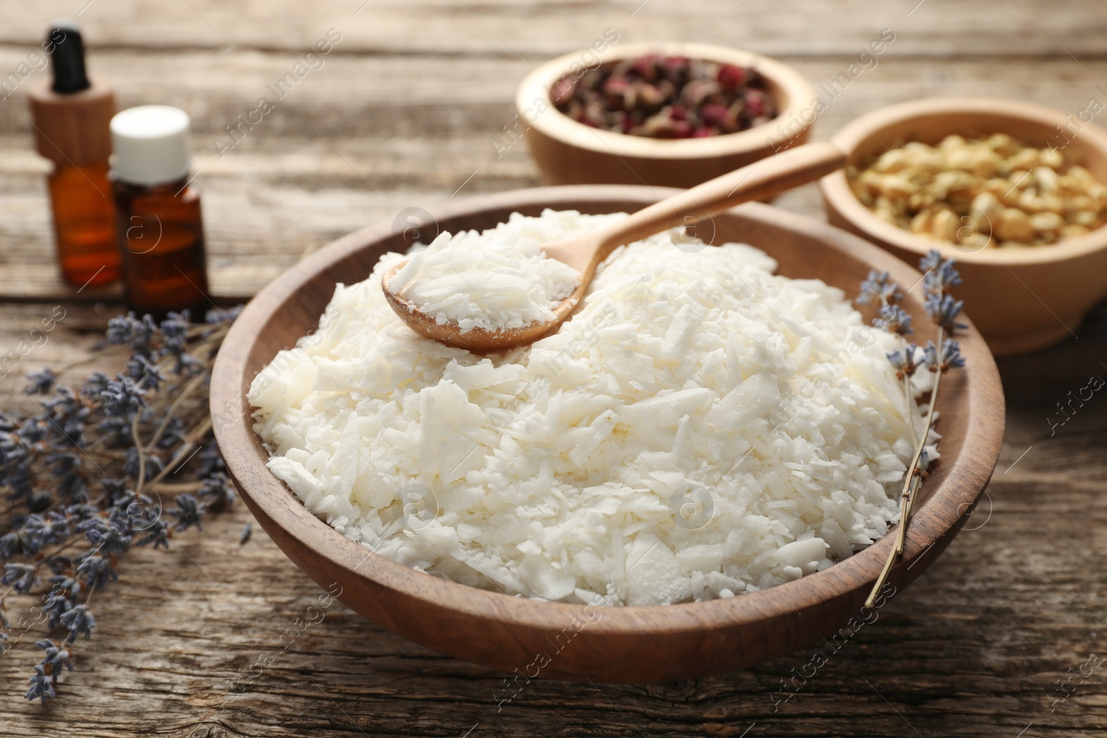 Photo of Soy wax in bowl and other different ingredients for making candles on wooden table, closeup