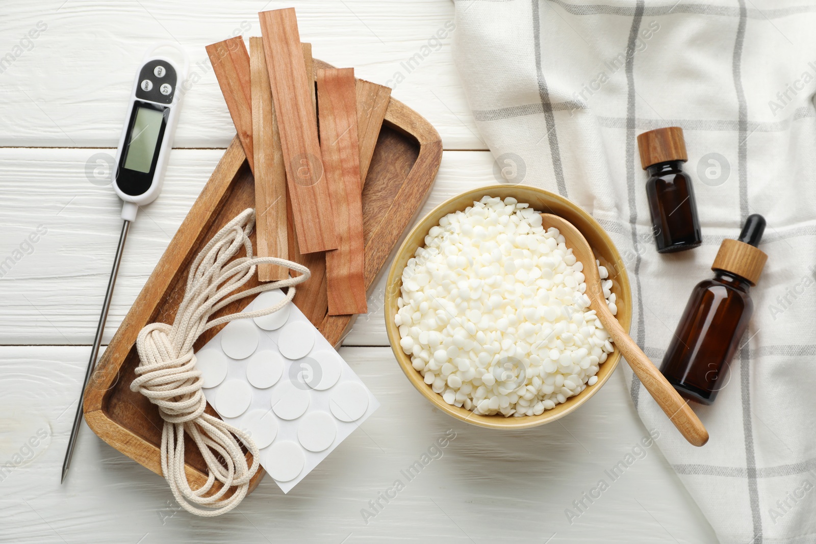 Photo of Soy wax in bowl, essential oils and different tools for making candles on white wooden table, flat lay