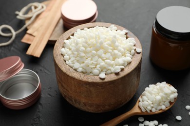 Photo of Soy wax in bowl, candle, wooden wicks, twine and jars on black table, closeup