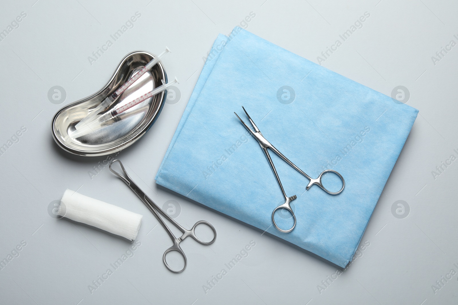 Photo of Different surgical instruments and gauze on light grey background, flat lay