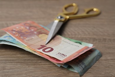 Photo of Euro banknotes and scissors on wooden table, closeup