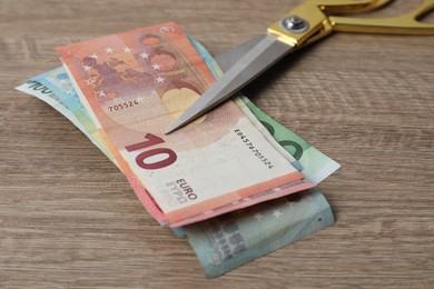 Photo of Euro banknotes and scissors on wooden table, closeup