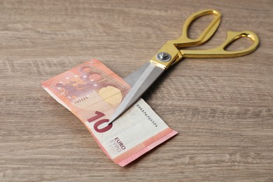 Photo of Euro banknotes and scissors on wooden table, closeup